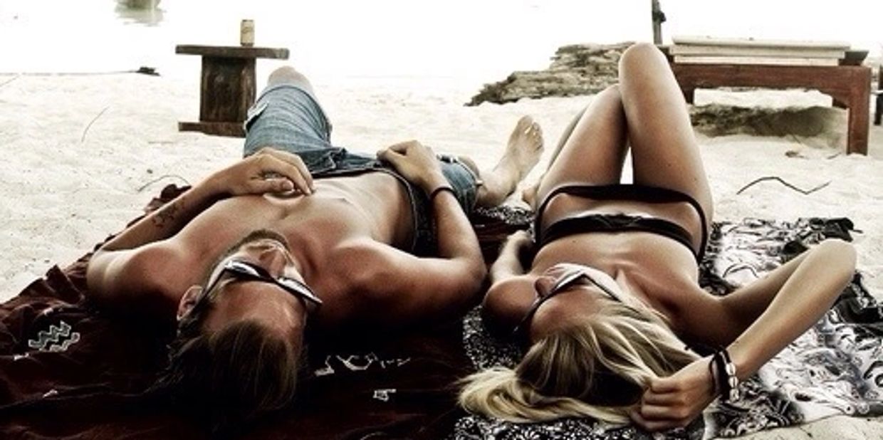 A couple relaxing on the beach wearing sunglasses and swimwear.